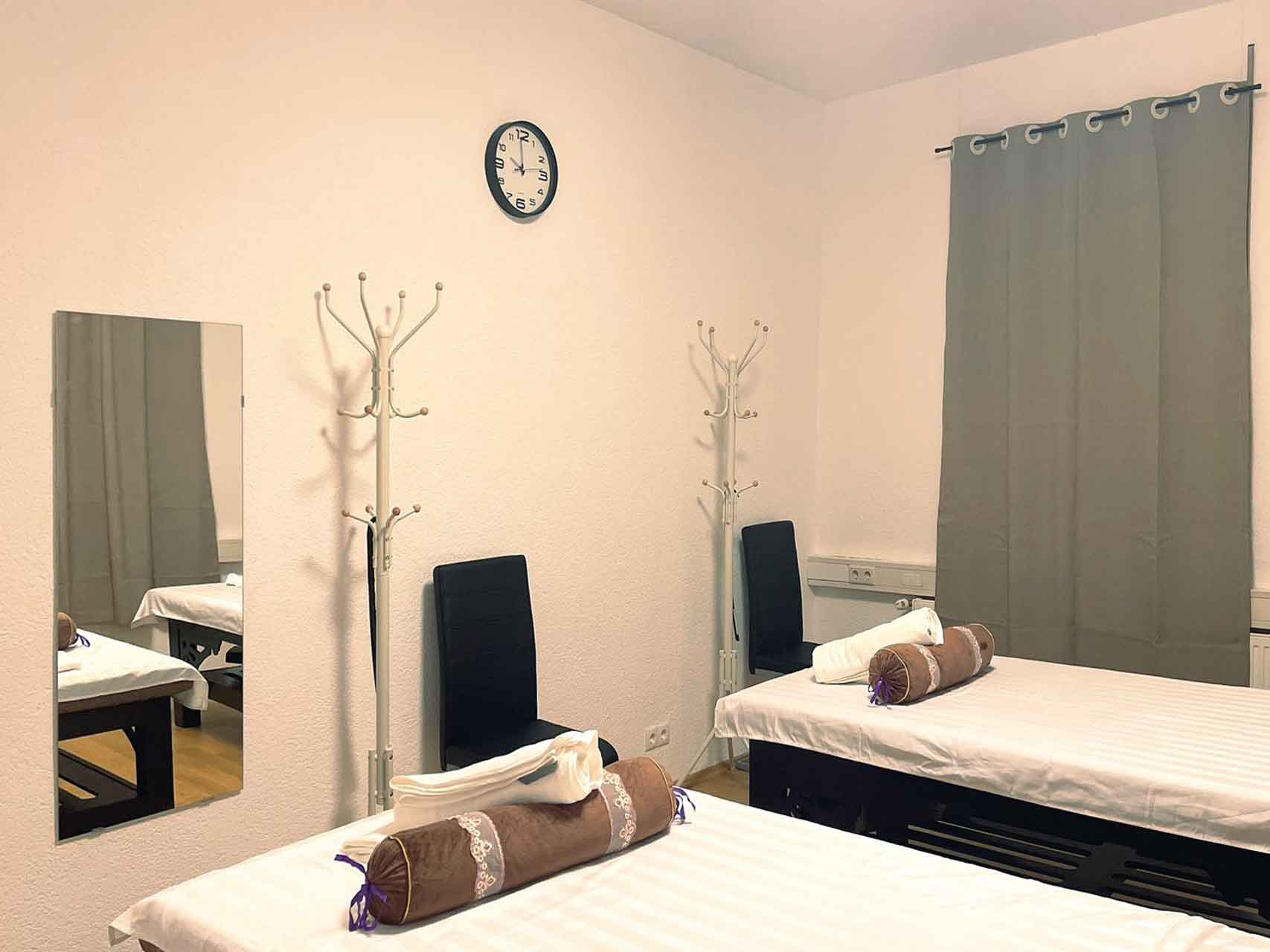 2 Behandlungsbetten von der anderen Seite, dahinter ein Vorhang und Bilder an der Wand